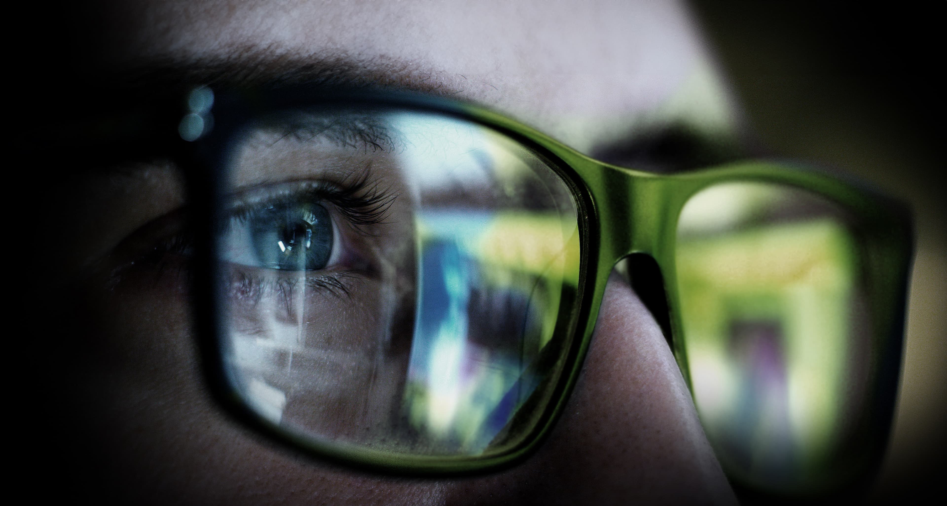 Nahaufnahme eines Auges hinter einer Brille, in deren Gläsern sich digitale Inhalte spiegeln.