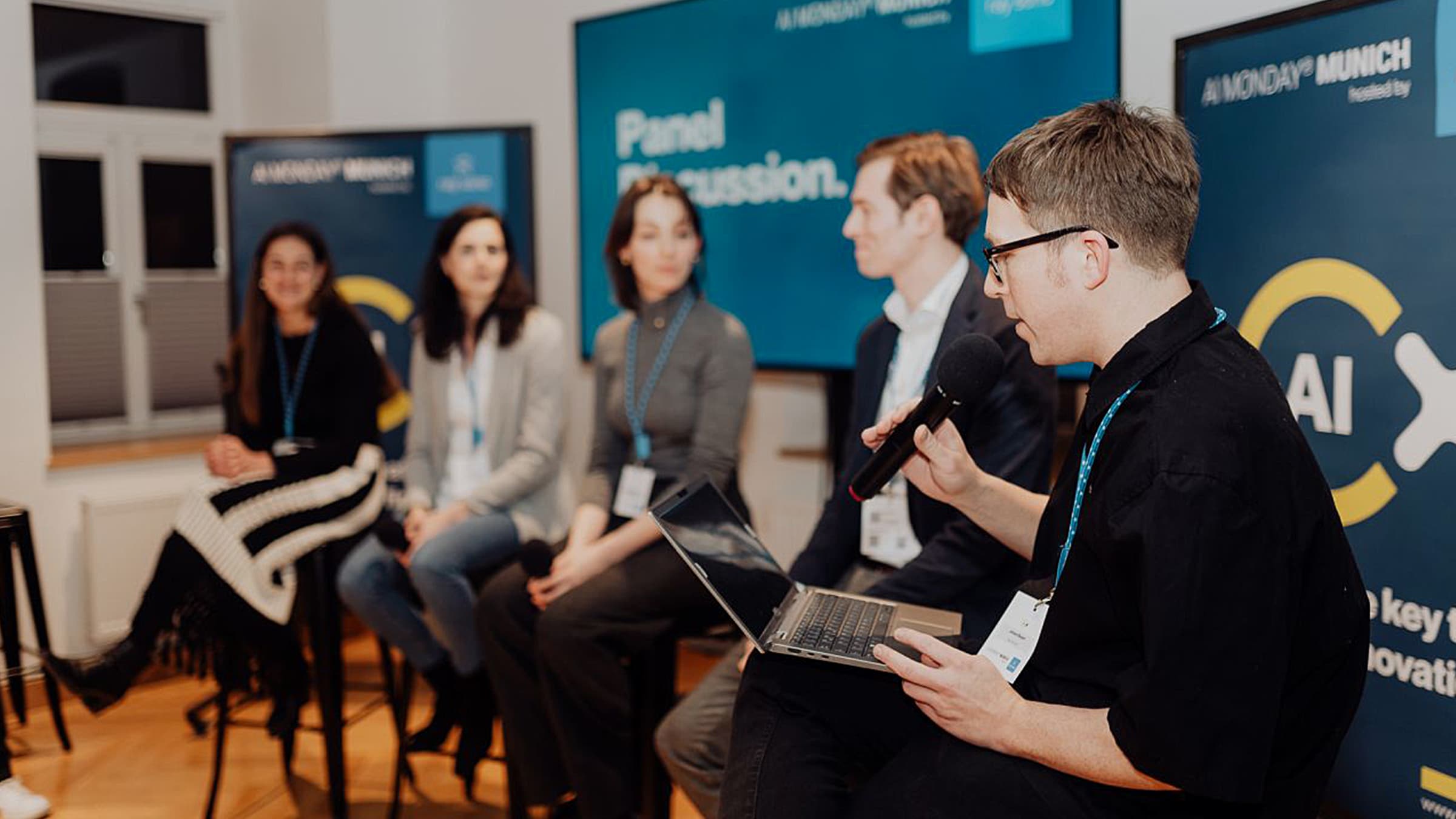 Paneldiskussion auf "AI Monday" in München. Johann Bayerl und Vortragende, Publikum im Hintergrund. Fokus auf KI-Innovationen.