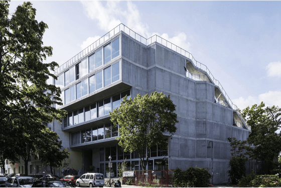 Ray Sono Office im Lobe Block in Berlin mit großen Glasfenstern an einer Straßenecke, umgeben von Bäumen und parkenden Autos.